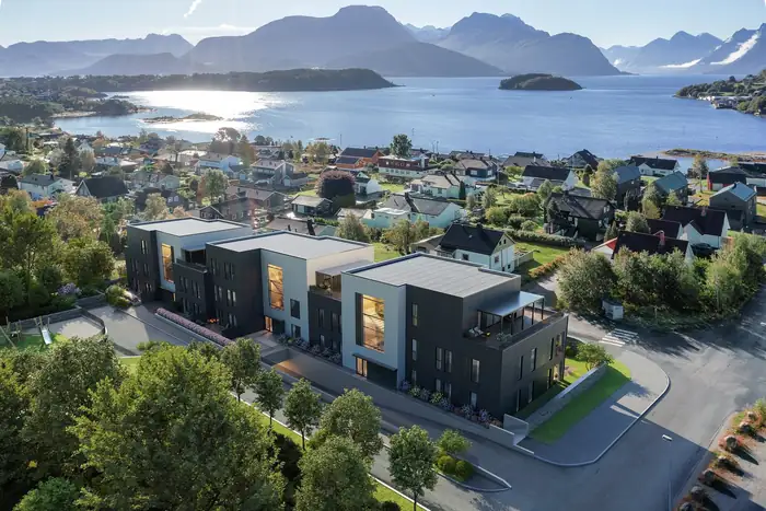 Tre moderne boligbygg ved fjorden, med fjell bak
