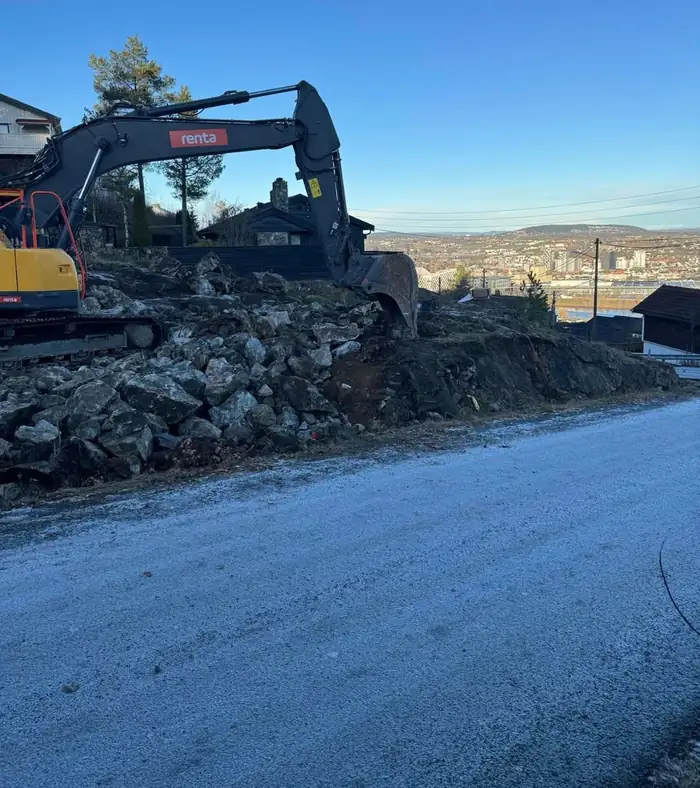 Gravemaskin graver ut tomten, med byen i bakgrunnen
