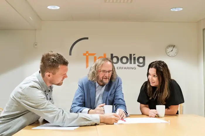 Tre personer i møte ved et bord foran Tid Bolig-logoen