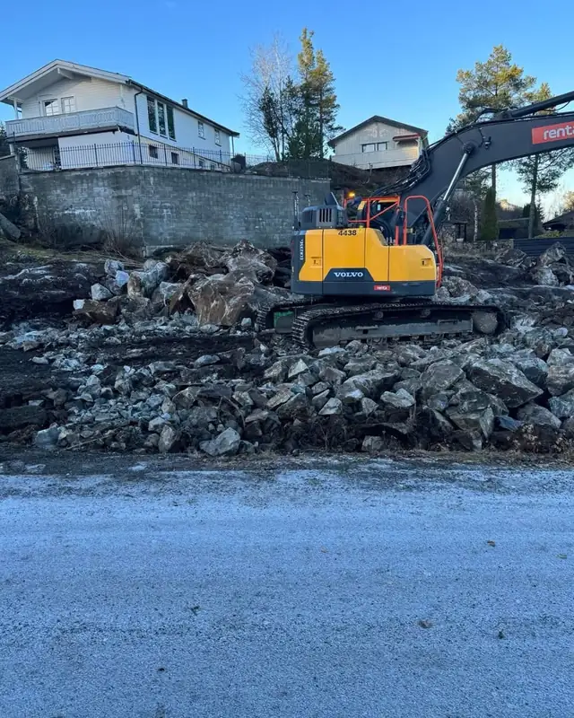 Gravemaskin rydder en tomt mellom eneboliger